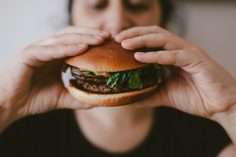 persona che tiene in mano un panino con hamburger in primo piano