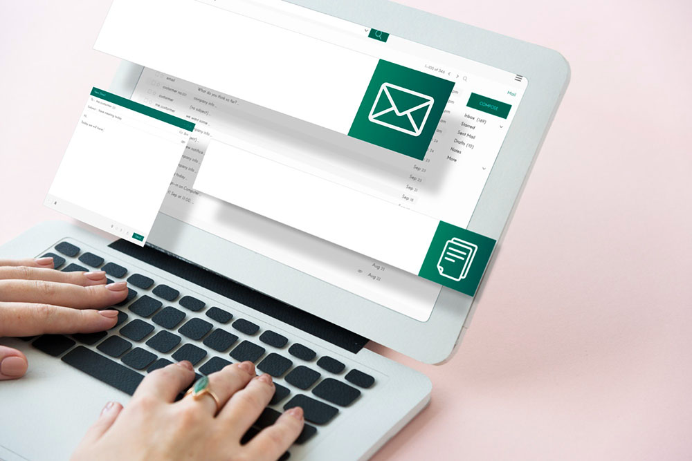 mani che digitano su un computer da cui escono schermate di email