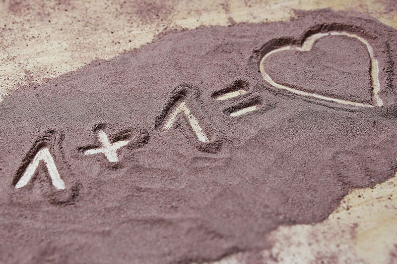 immagine scritta in sabbia rosa "1+1=cuore"
