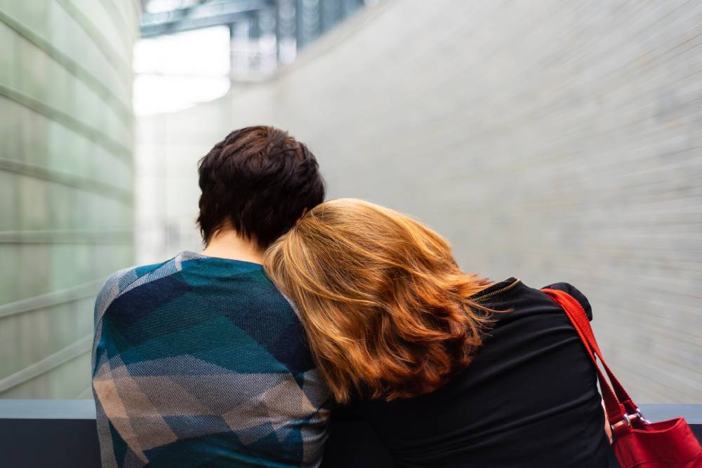 due persone di schiena, la donna sulla destra appoggia la testa sulla spalla della persona sulla sinistra