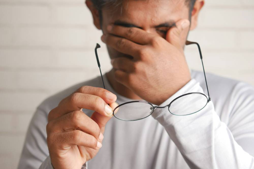 uomo con mani sugli occhi e occhiali in mano