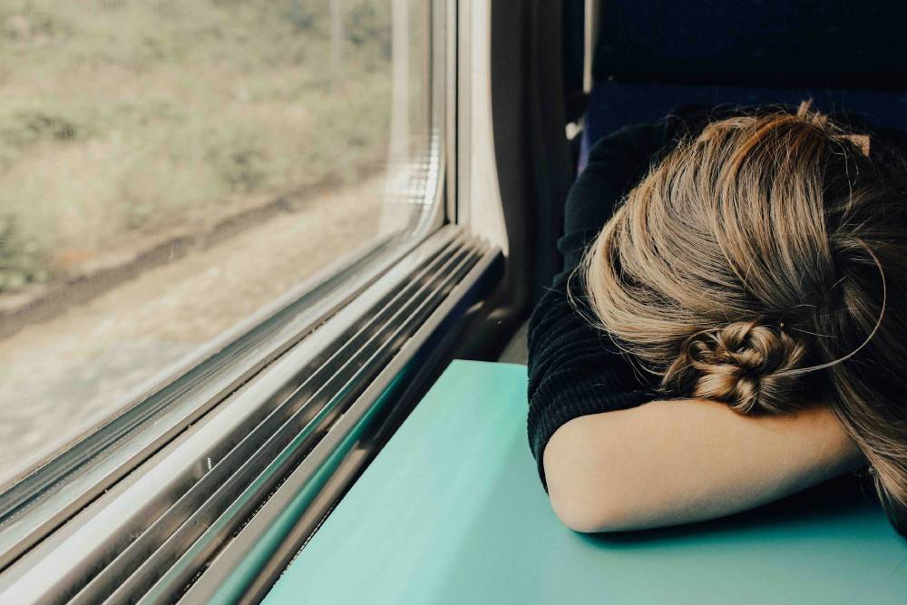 donna con faccia appoggiata ad un braccio distesa in avanti su un tavolino del treno