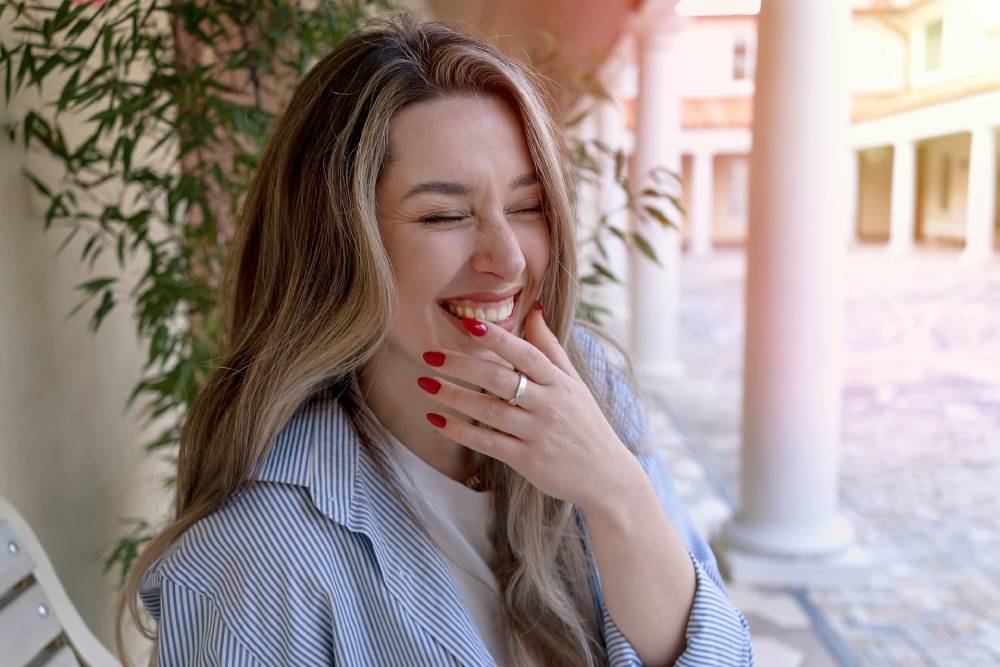 primo piano di donna bionda che porta una mano alla bocca e ride